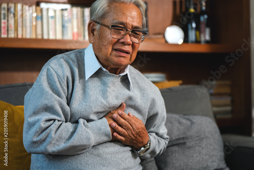 Foto Senior man sits on sofa while hand on chest