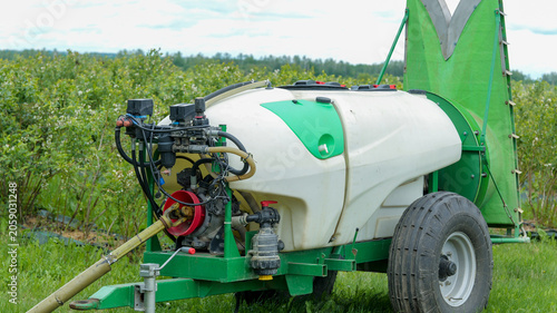 фотографія Agricultural sprayer with large tank and boom in a field of green bushes