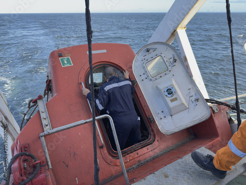 Fotografie cargo vessel crew members entering free fall life boat during abandon ship drill