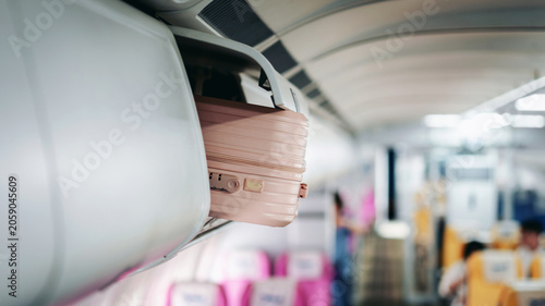Schilderij op canvas Traveler stows pink carry on suitcase in overhead bin airplane c