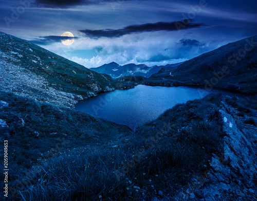 mysterious summer scenery of alpine capra lake with steep slopes at night. fantasy view of transylvania alps, sibiu county. full moon over southern carpathian mountains of romania travel background