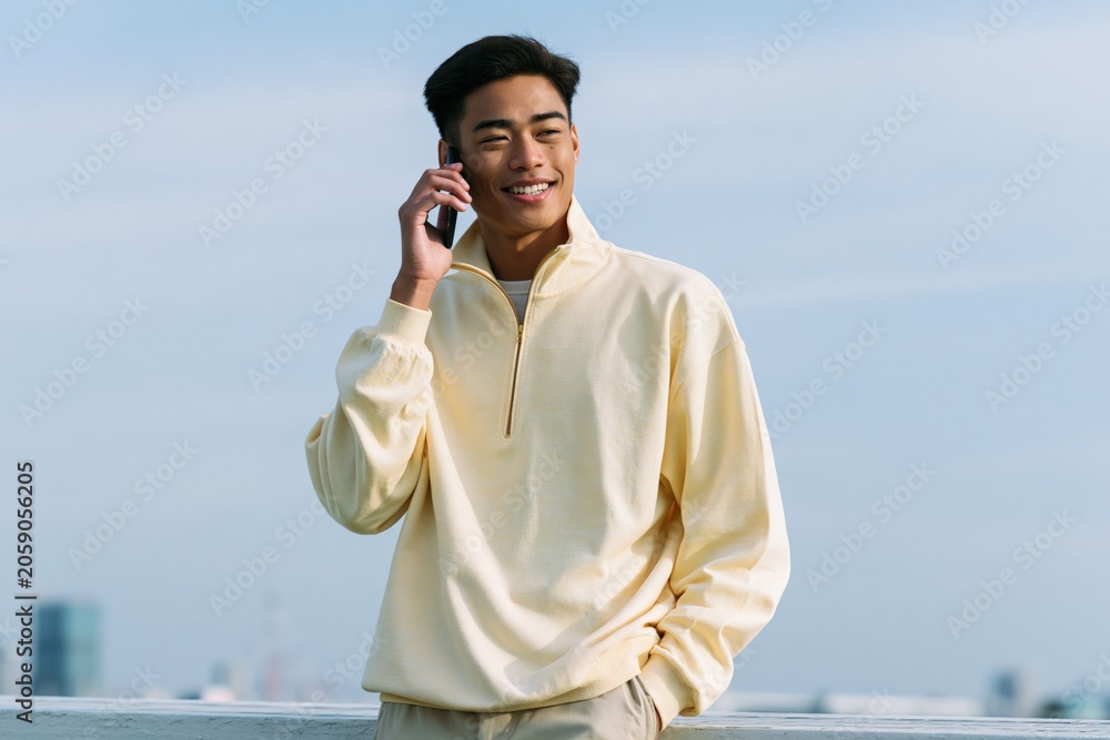 Obraz premium Smiling young man using smartphone on rooftop in a light yellow quarter zip sweater for casual banner and website hero background