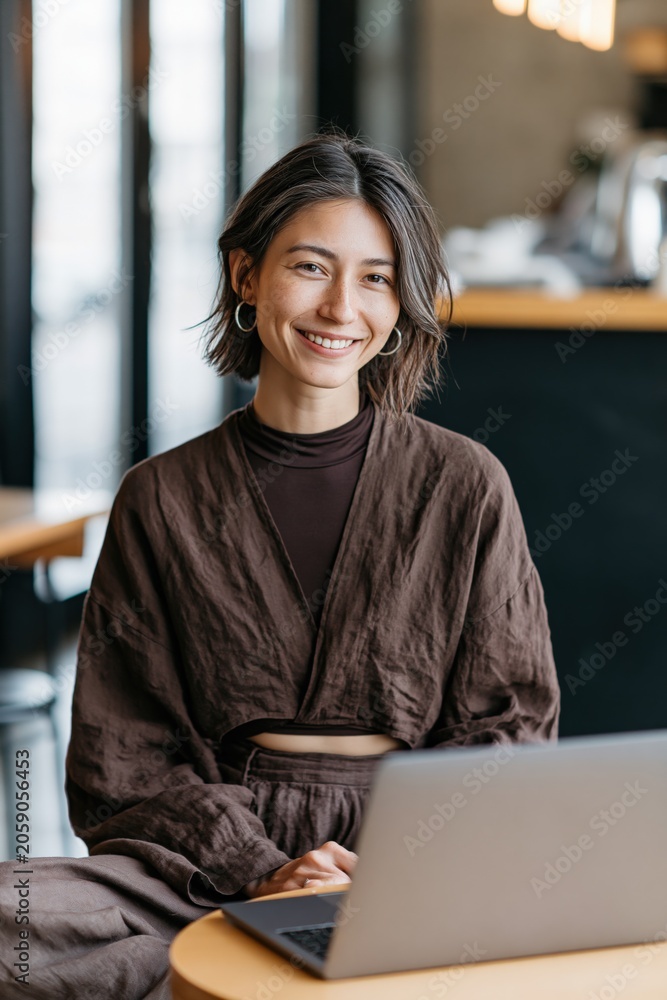 Fototapeta premium Smiling woman working on laptop in cozy cafe wearing brown outfit for business profile banner and social media background