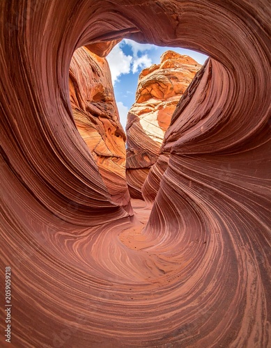 A swirling, sandstone formation with a heart-shaped opening revealing a blue sky