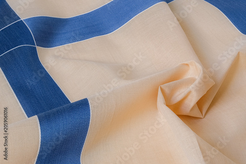 A macro close-up showcasing the delicate fabric texture, weave, and soft folds of a beige and blue cross-patterned textile handkerchief.