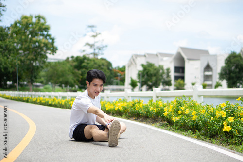 Obraz na plátne A young man in a white sports outfit is stretching his leg and ankle muscles to loosen them up before or after running