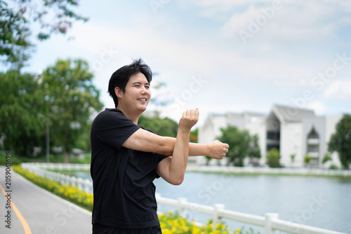 A muscular young man wearing a black T-shirt is stretching one arm across his side and crossing the other arm to warm up his shoulder muscles.