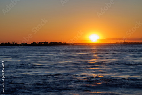 Sunset glowing on the horizon over rippling water at dusk
