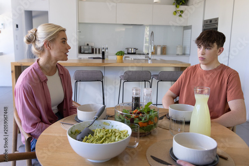 Mother and teenage son talking while sitting at kitchen dining table with green pasta