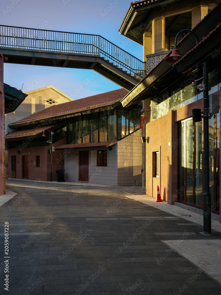 Fototapeta premium Empty paved street with elevated metal walkway connecting renovated buildings in bright daylight