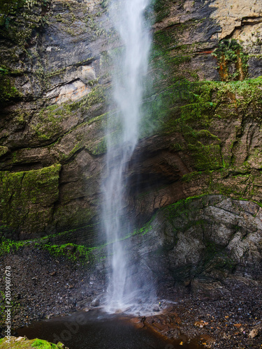 The majestic cascade of a powerful waterfall descends a lush, moss-covered cliff, a serene natural wonder in the vibrant landscapes of Peru