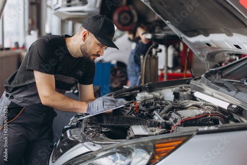 Bild auf Leinwand Mechanic performing car diagnostic and maintenance service, writing notes on cli