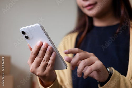A woman in a yellow cardigan uses her smartphone to browse social media or an app.