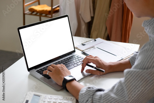 An Asian business owner types on a laptop with a blank white mockup screen at his desk