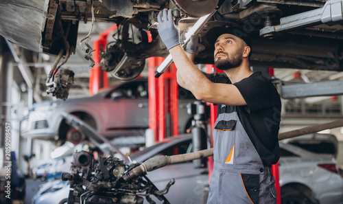 Male technician inspecting an automobile's undercarriage with a flashlight, working in an auto service station