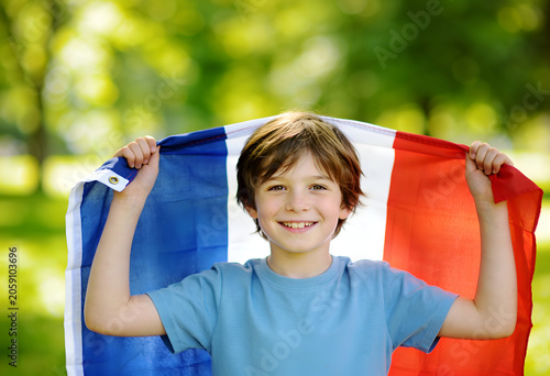 Happy young boy holding a French flag in a green outdoor setting