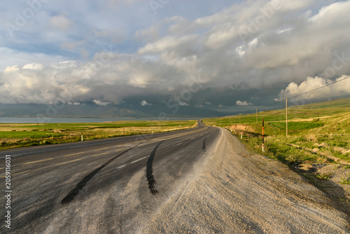 Winding asphalt road through rural landscape under cloudy sky. Road safety concept.