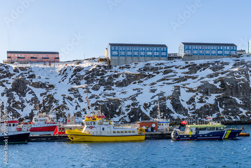 Fishing boats in the harbor below colorful houses on a snowy rocky hillside in Nuuk, Sermersooq, Greenland