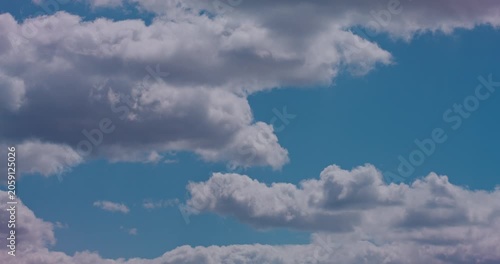 Bright cumulus clouds drifting across a calm blue sky in soft daylight