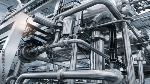Industrial piping system in monochrome. Stainless steel pipes form complex network. Visible valves and connections in factory setting. Clean technical photography