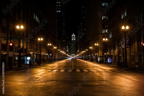 Empty urban street at night with wet pavement reflecting city lights and illuminated buildings