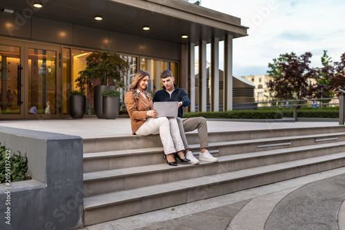 Young professionals collaborating on laptop outside modern office building