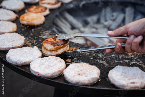 Obraz na plátně Grilled round meat patties being flipped on a large outdoor griddle with tongs