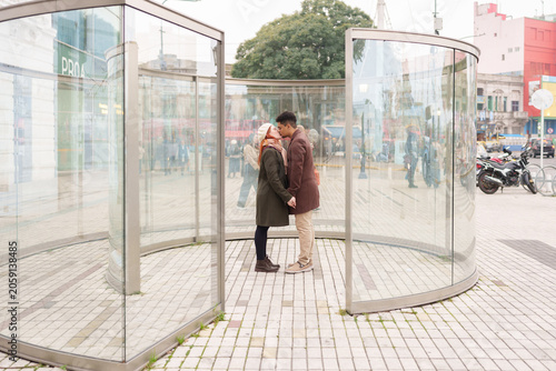 Young couple sharing a kiss inside a modern public glass art installation in the city