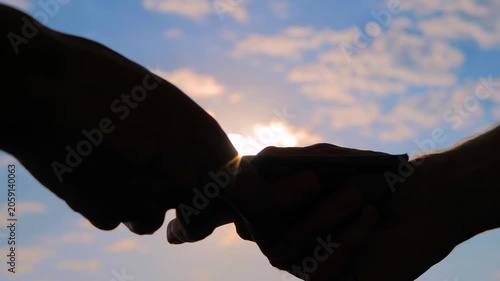 Woman is counting dollar bills. Hands silhouettes with money, banknotes against the sunset, sunrise sky with sun lens flares, close up view. One person is giving a bribe to another person.