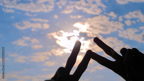 Silhouettes of woman hands are showing victory sign, gesture of peace against the sunset or sunrise sky - close up, sun lens flare. Unity, harmony and positive concept
