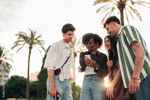 Quadro su tela Diverse young friends smiling and looking at a smartphone screen, sharing a mome