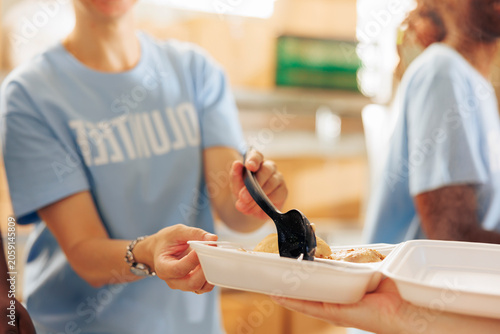 Quadro su tela At charitable food drive, caucasian lady is shown offering a warm meal to a disadvantaged hungry homeless person; a close-up of a team of humanitarian relief workers distributing free food