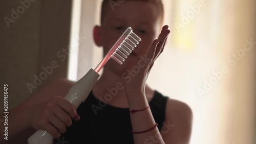 A teenager uses a Darsonval device. The young man runs his hand over the glass attachment designed for hair. Professional skincare at home. Teenage skin issues during hormonal changes