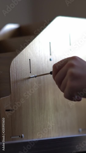 A teenager assembles a bookshelf. The child tries on the parts to assemble the furniture. Inserts a screw into the hole and tightens the parts