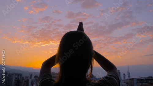 Silhouette of woman is lifting hands up, doing stretching and yoga exercises against the dramatic sunset, sunrise sky - sun salutation. Fitness, early morning, sport and freedom concept