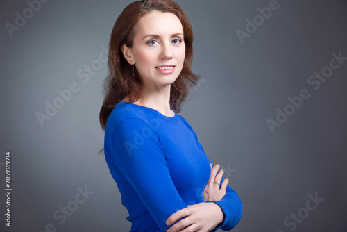 Close-up Portrait of Positive Winsome Mature Caucasian Business Woman in Blue Jumper With Folded Hands Against Dark White Background