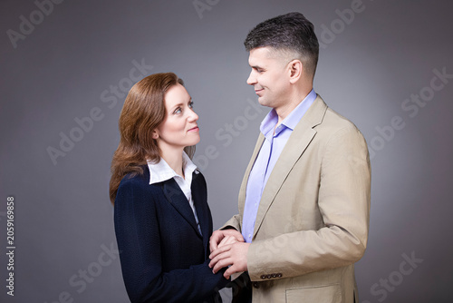 Portrait of Loving Caucasian Mature Loving Couple Posing in Business Suits Together Embraced Over Gray Backround As Family People in Business