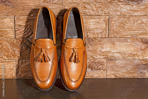 Tan Tassel Loafers Shoes Made of Calf Leather with Leather Sole Placed On Wooden Surface Against Grunge Wall Background