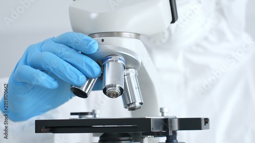 Foto Close up of virologist's hands in blue gloves adjusting microscope in laboratory, conducting scientific research and analysis