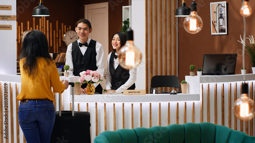 Fotografie Front desk team greeting guest at five star hotel reception, welcoming person and ensuring easy check-in procedure, woman client entering lobby with luggage, hospitality industry