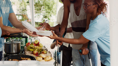 Fotografija Voluntary individuals contributes to and offers humanitarian help to the underprivileged and needy, young black volunteer woman helps African American guy using crutches at a food drive