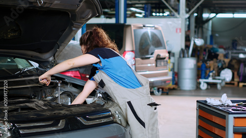 фотографія Diligent mechanic in garage using torque wrench to tighten studs inside opened up vehicle after changing oil, auto repair shop employee doing maintenance on car, wiping leftover mess