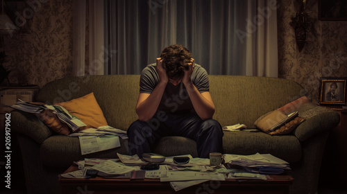 Man sitting on sofa with head in hands surrounded by unpaid bills ,alone man, refusal to eat, man sitting on the sofa, a man working in the evning in empty flat, sad man playing in