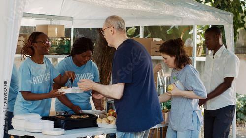 Quadro su tela At homeless shelter, warm and welcoming female volunteers cheerfully provide the less fortunate with complimentary meals, poor and needy individuals receives food contribution from hunger relief team