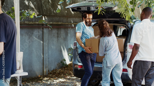 Konstfotografi Less fortunate Caucasian woman and African American man are seen accepting donation box from male volunteer at a food drive, charity worker distributes essentials to the needy and homeless people