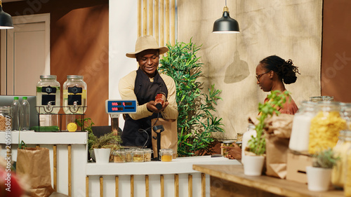 фотографія African American woman bringing natural products at checkout, talking to vendor about healthy eating while he scans goods, local farmer selling his homegrown veggies and homemade items