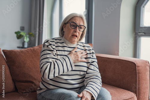 Foto Senior woman suffering from severe sudden chest pain or heart attack while sitti