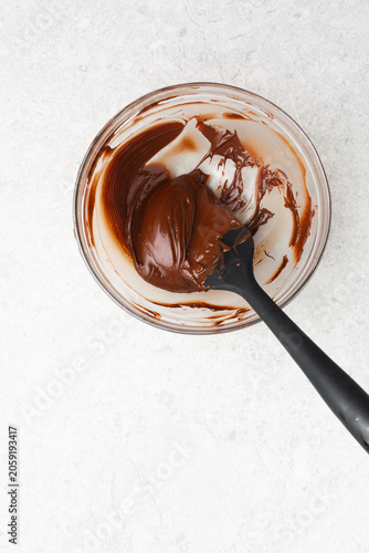 Overhead view of melted dark chocolate on a glass bowl on a white countertop, top view of melted chocolate for baking