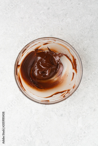 Overhead view of melted dark chocolate on a glass bowl on a white countertop, top view of melted chocolate for baking
