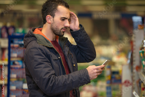 Obraz na płótnie Man Looking Confused At Mobile Phone In Supermarket